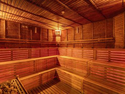 Holzsauna mit mehrstufigen Sitzbänken und sanfter Beleuchtung, warmes, rotes Licht erzeugt Atmosphäre.