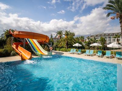 Piscina con scivoli d'acqua, lettini e palme in un resort alberghiero sotto il sole.