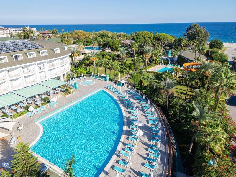 Großer Hotelpool mit blauen Liegestühlen, Palmen und Meer im Hintergrund an sonnigem Tag.