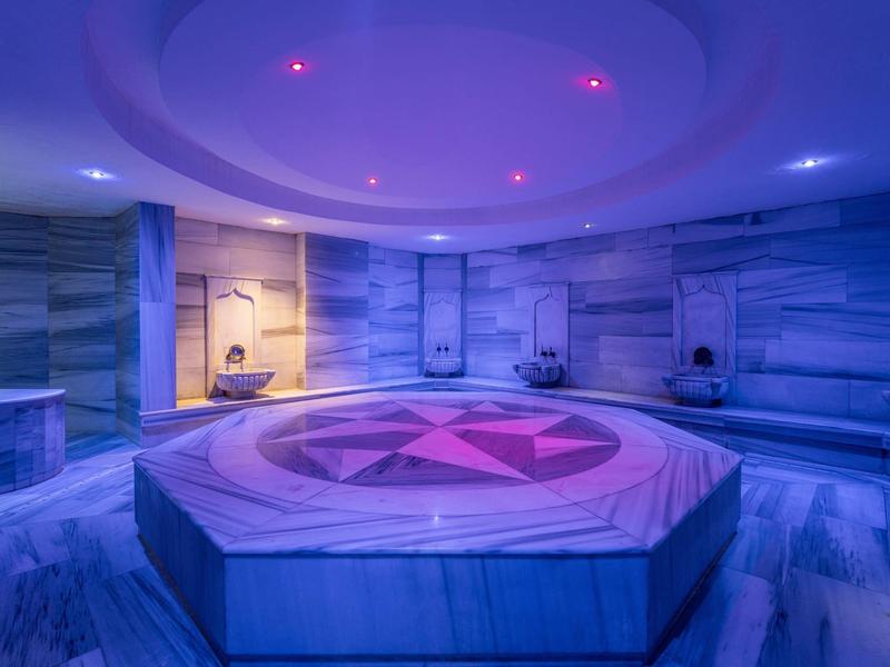 Moderner runder Hamam mit blauen Marmorwänden, zentralem achteckigem Tisch und violetter Beleuchtung.