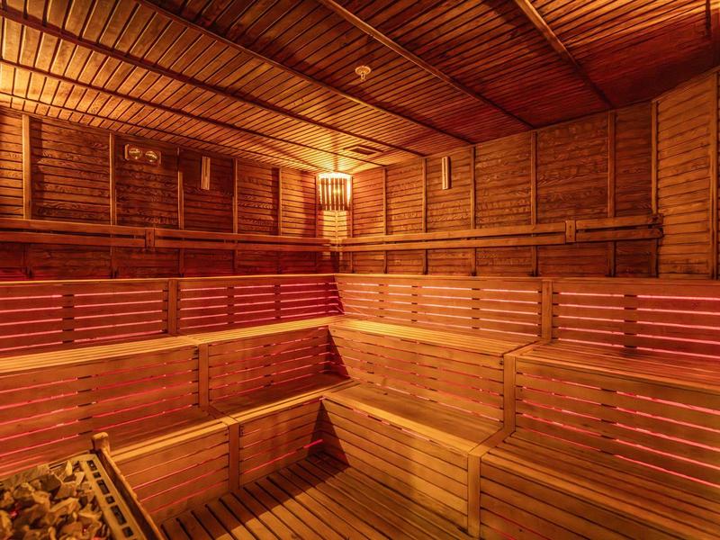 Holzsauna mit mehrstufigen Sitzbänken und sanfter Beleuchtung, warmes, rotes Licht erzeugt Atmosphäre.