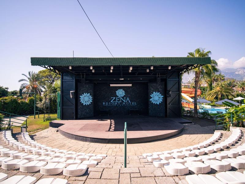 Freiluftbühne mit halbrundem weißen Sitzbereich, Palmen und klar blauem Himmel im Hintergrund.