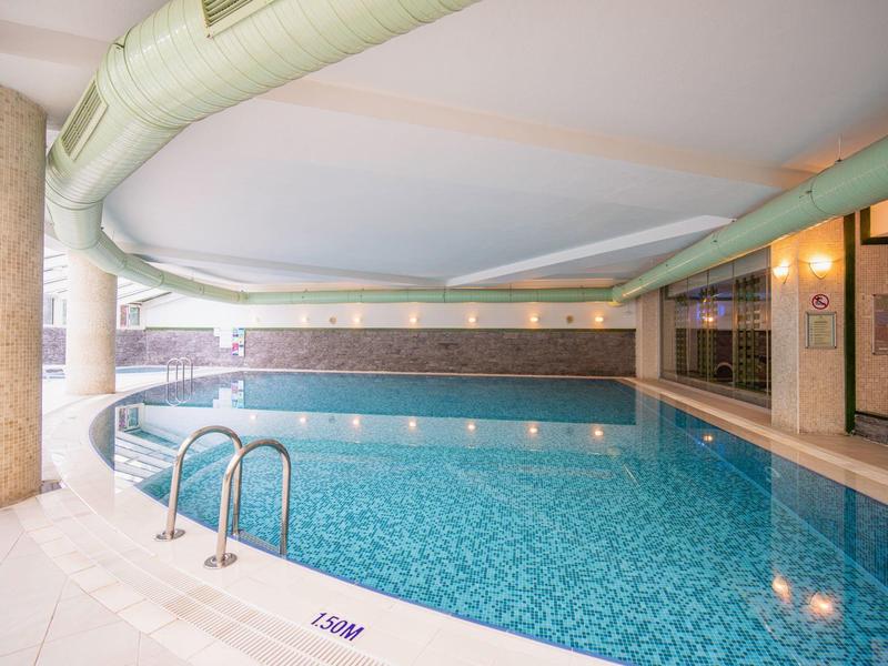 Innen Schwimmbad mit klarem blauem Wasser, weißen Fliesen und Warmlicht-Ambiente.