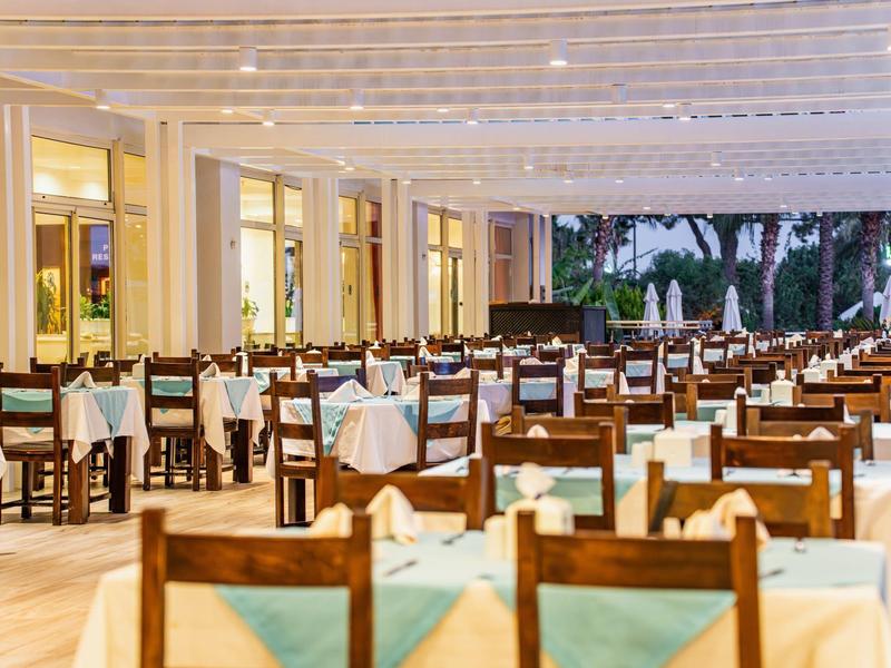 Großer Speisesaal mit vielen Holztischen und Stühlen, gedeckt mit weißen Tüchern und blauen Servietten.