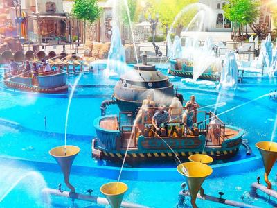 Kinderen spelen met kleine bootjes in een kleurrijke, verlichte fontein met waterstralen.