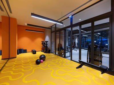 Moderne fitnessruimte met gele vloer, gewichten en fitnessapparatuur achter glazen wanden.