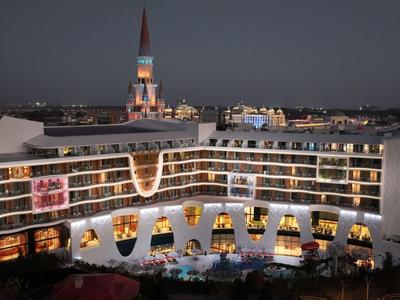Modern hotel met verlichte balkons en zwembadgebied in een stad 's nachts.