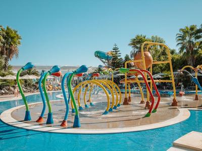 Kleurrijk waterspeelgebied met glijbanen en fonteinen in een tropisch hotelzwembad bij zonnig weer.