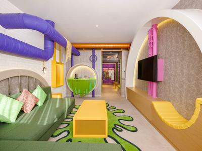 Kleurrijke hotelkamer met groene bank, gele tafel en ronde kleurrijke accenten.