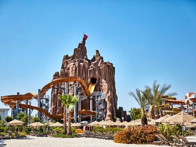 Waterpark met tropische planten, glijbanen en een rotsachtige vulkaan op de achtergrond