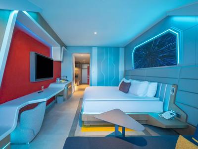 Modern hotelkamer met groot bed, bureau, tv en blauwe sfeerverlichting.