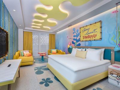 Kleurrijke hotelkamer met groot bed, bank, unieke plafondverlichting en vrolijke wanddecoratie.