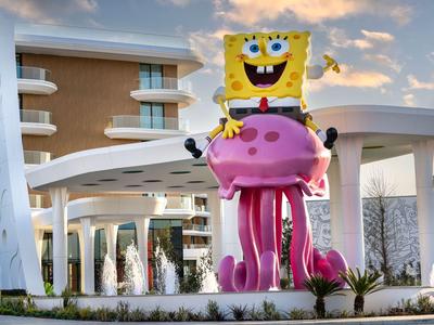 Große bunte SpongeBob-Figur vor modernem Hotelgebäude im Abendlicht.