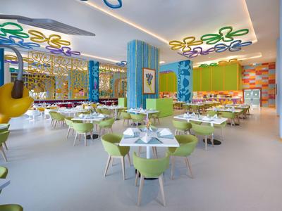 Hell gestalteter Hotelrestaurant mit grünen Stühlen und bunten Deckenlichtern.