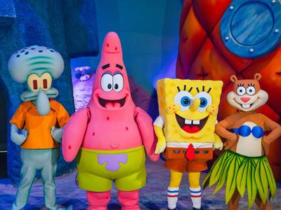 Vier bunte Charakterfiguren aus SpongeBob stehen in einem farbenfrohen, ozeanischen Hintergrund.