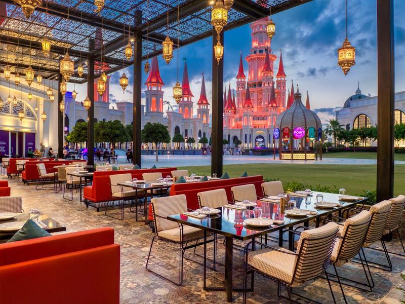 Openluchtrestaurant met rode fauteuils en uitzicht op een verlicht kasteel bij schemering.