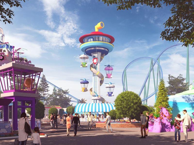 Uitzicht op een pretpark met carrousel en achtbaan onder een blauwe hemel.