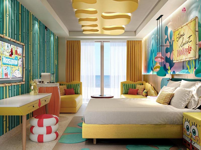 Kleurrijke hotelkamer met levendige lampen, zitgelegenheden en groot raam met zeezicht.
