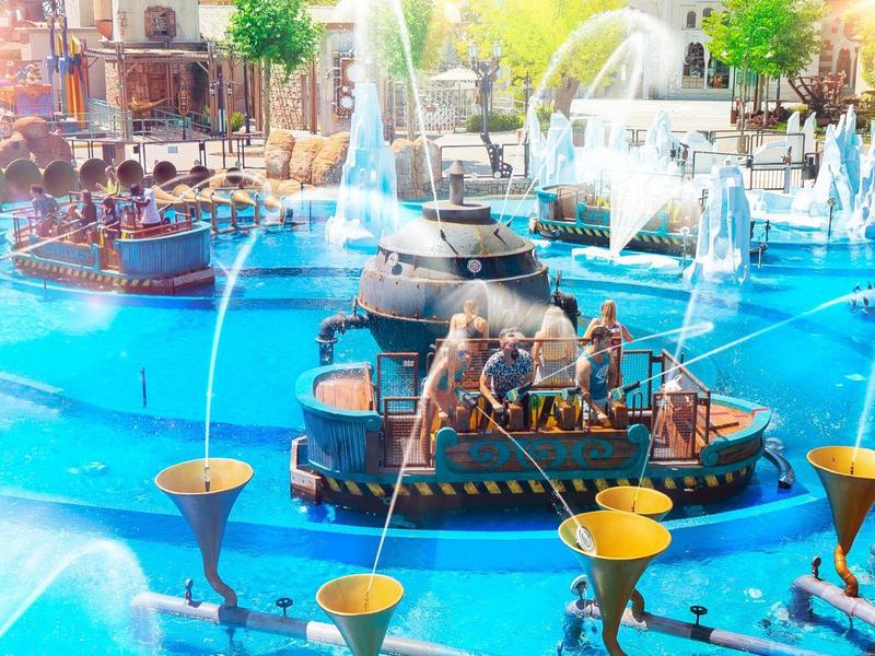 Kinderen spelen met kleine bootjes in een kleurrijke, verlichte fontein met waterstralen.