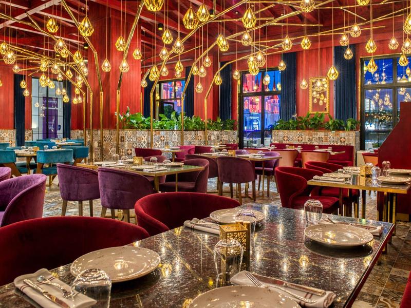 Luxueus restaurant met rood en paars interieur, kroonluchters en gedekte tafels.