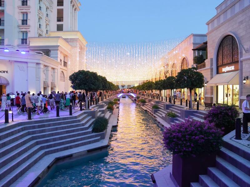 Levendige kanaal met trappen en bomen, omgeven door hotels en restaurants bij avondlicht.