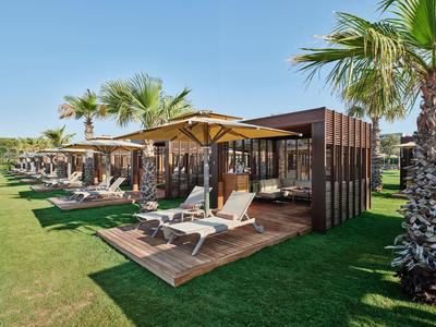 Bungalows d'hôtel modernes avec terrasses en bois, transats et parasols sur une pelouse bien entretenue.