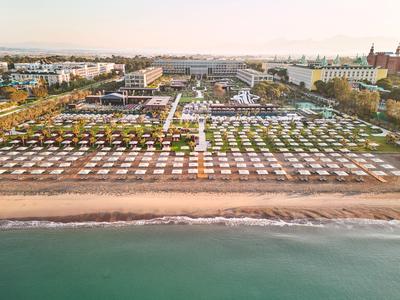 Plage avec de nombreux parasols blancs, bâtiments traditionnels et mer calme en arrière-plan.