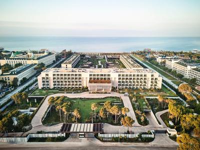 Hôtel moderne avec grande entrée, jardins paysagers et vue sur la mer en arrière-plan.