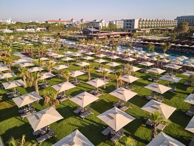 Rangées ordonnées de parasols sur pelouse verte devant un complexe hôtelier côtier.
