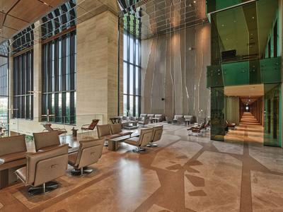 Hall d'hôtel moderne avec de grandes fenêtres, fauteuils confortables et éclairage chaleureux.