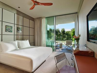 Chambre d'hôtel moderne avec grand lit, verre et vue sur terrasse et jardin.