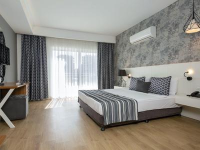 Modernes Schlafzimmer mit großem Bett, grauer Akzentwand, Holzfußboden und viel Tageslicht.