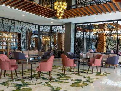 Espace lounge élégant d'hôtel avec des fauteuils roses, des tables et un tapis décoratif.