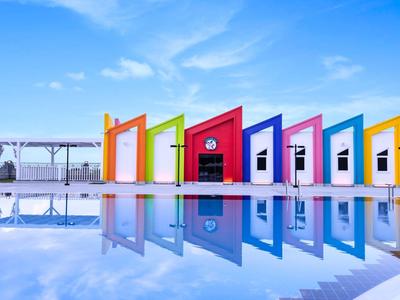Cabines colorées au bord d'une piscine avec ciel bleu clair et reflet dans l'eau.