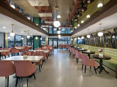 Salle à manger moderne avec des chaises roses, des murs verts et de grandes fenêtres laissant entrer la lumière du jour.