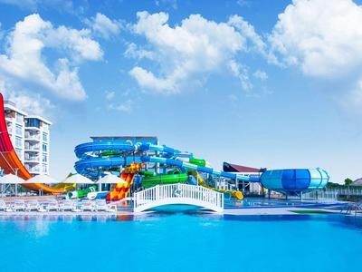 Water park with colorful water slides and large blue pool under blue sky.