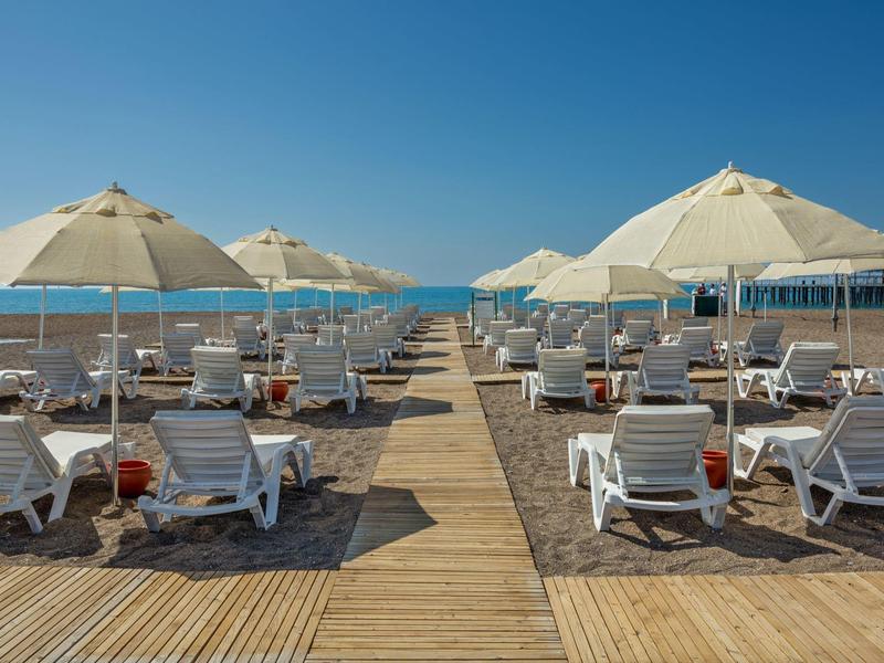 Plage avec chaises longues et parasols blancs face à une mer bleue sous un ciel clair.