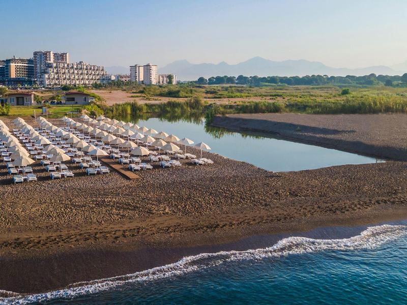 Plage isolée avec chaises longues et hôtel en bord de mer sous un ciel clair.