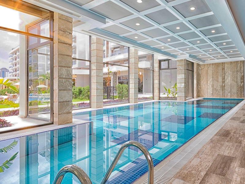 Piscine intérieure moderne avec grandes fenêtres donnant sur un jardin.