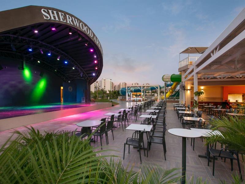 Grande scène extérieure avec de nombreuses tables et chaises pour les invités au coucher du soleil.