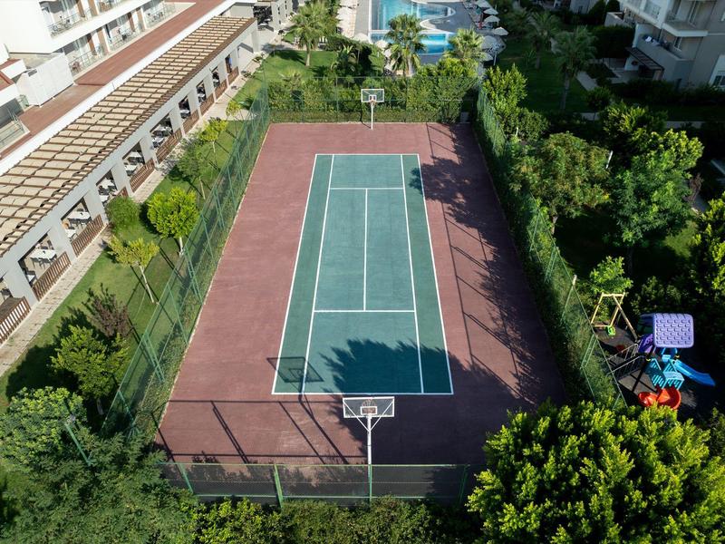 Vue aérienne d'un court de tennis à côté d'un hôtel avec arbres et aire de jeux