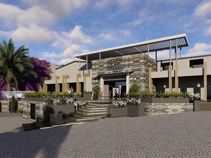 Hotel moderno con terrazza, palme e piazzale lastricato sotto un cielo nuvoloso.