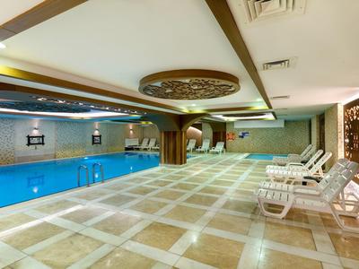 Helles Hallenbad mit blauen Wasser, cremefarbenem Boden und weißen Liegen an einer Wand.