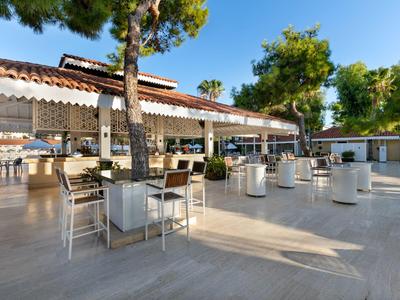 Ristorante all'aperto dell'hotel con sedie e tavoli bianchi sotto gli alberi alla luce del sole.