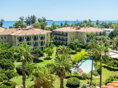 Hotel con due edifici su più piani circondati da palme, vegetazione rigogliosa e piscina con vista sul mare.