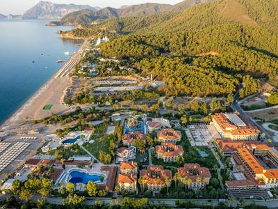 Küstenlandschaft mit Sandstrand, Hotels, bewaldeten Hügeln und blauem Meer bei klarem Himmel.