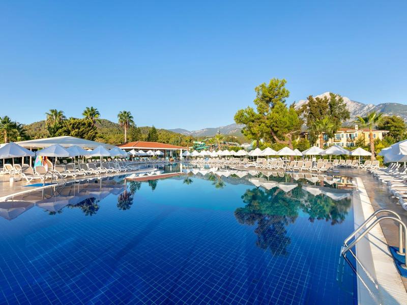 Großer blauer Pool umgeben von weißen Liegestühlen und Sonnenschirmen unter klarem Himmel.