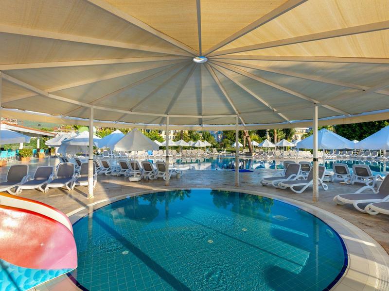 Überdachter Außenpool mit Sonnenliegen und buntem Wasserrutschenbereich am Rand.