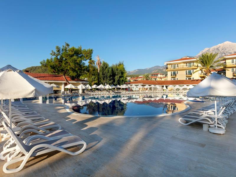 Großer Poolbereich mit vielen weißen Liegestühlen und Sonnenschirmen unter blauem Himmel.