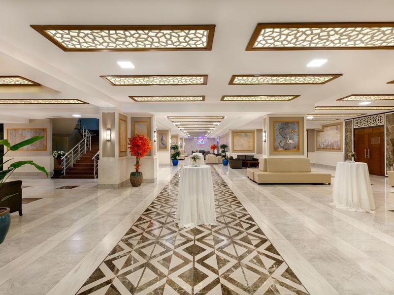 Großer heller Empfangsbereich mit gemustertem Boden, beigen Sitzgruppen und dekorativen Deckenlampen.